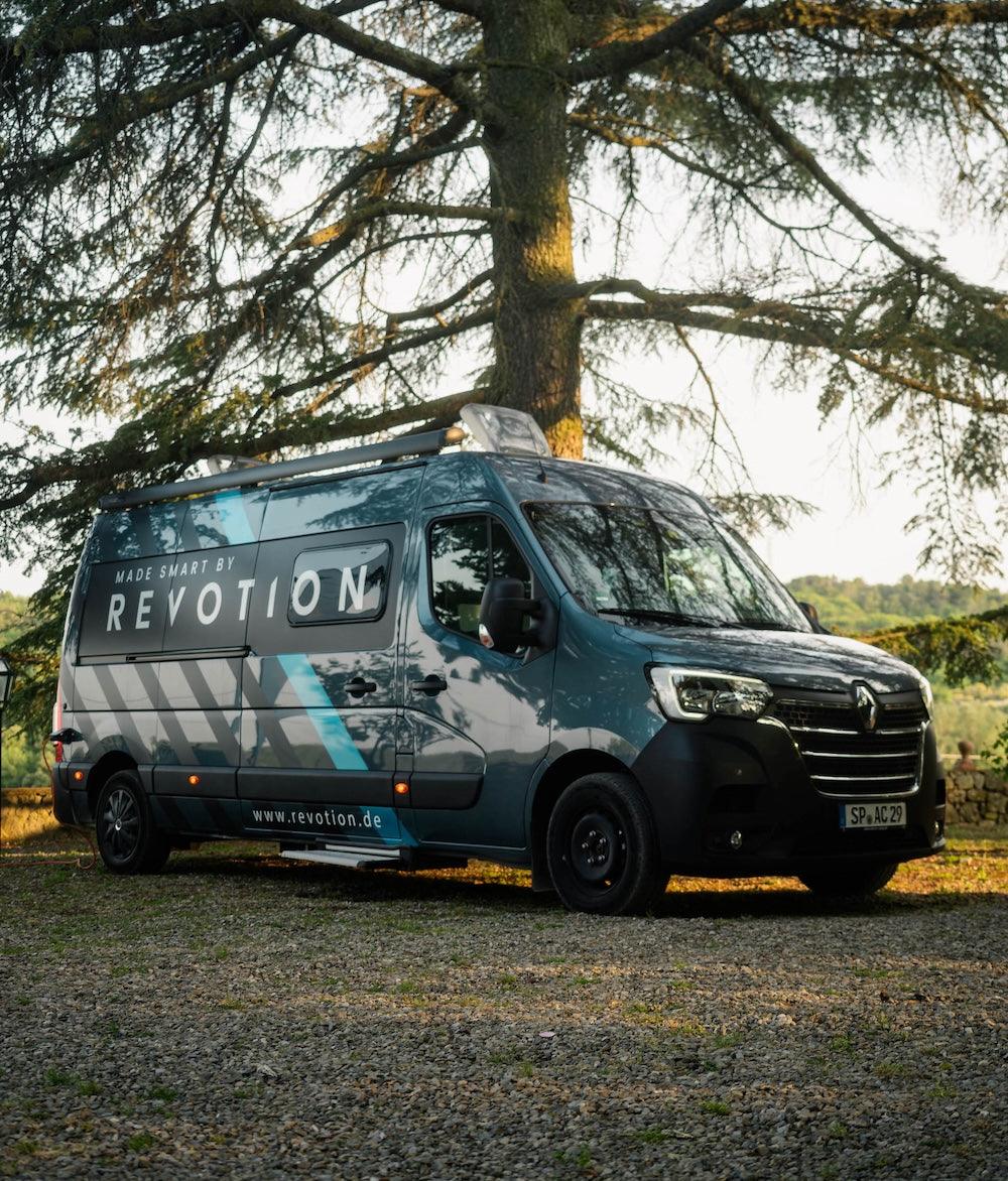 Grey and blue Campervan in front of a tree with landscape